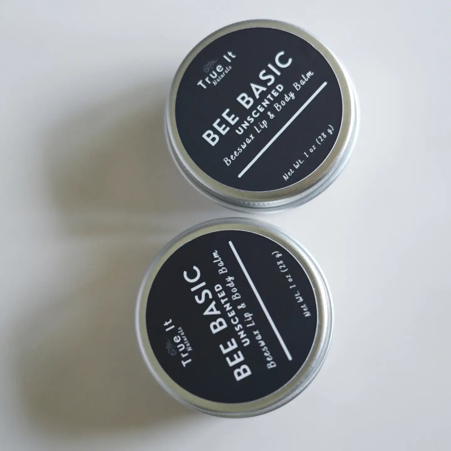Two containers of True It Naturals Bee Basic Unscented Lip & Body Balm from local beeswax on a light background