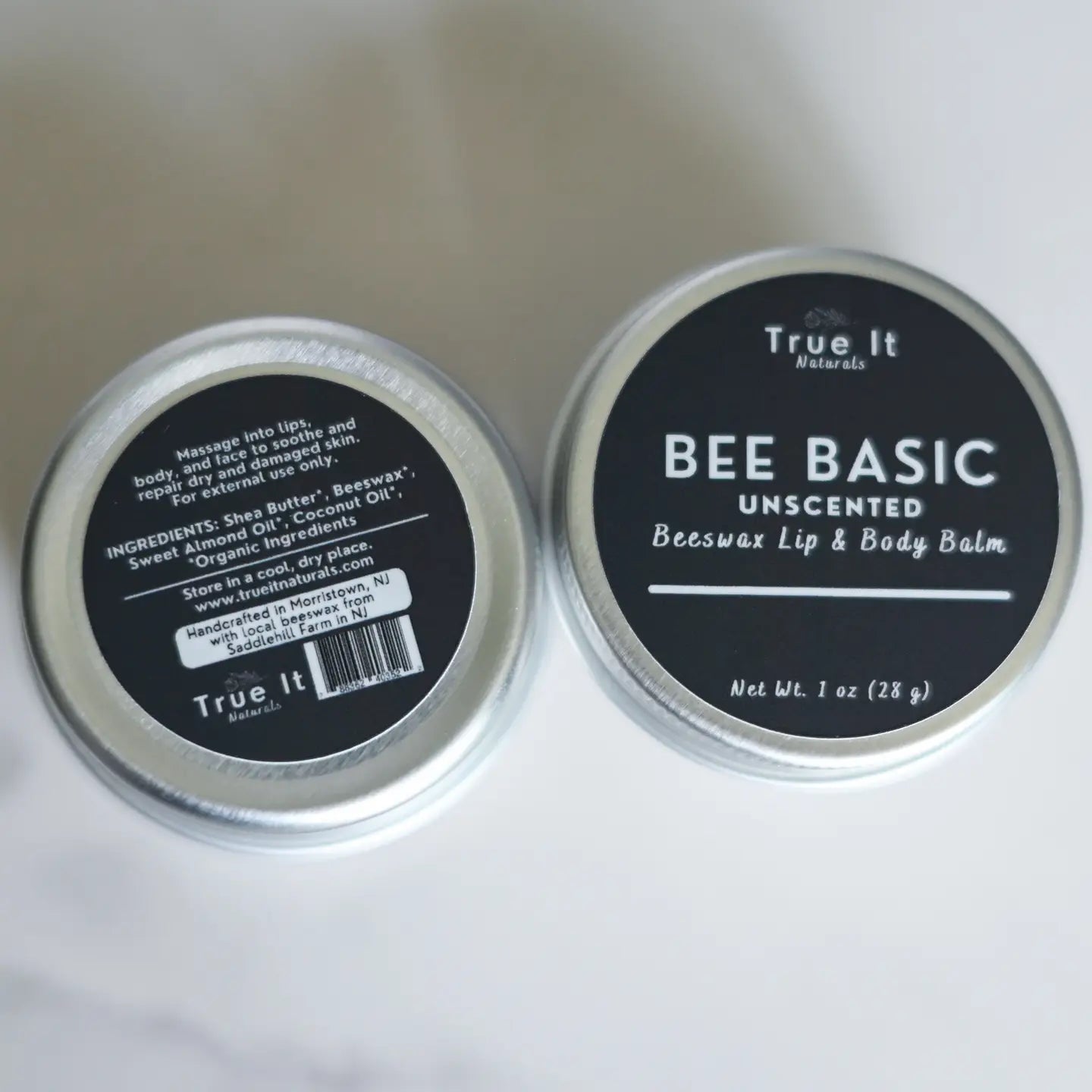 Two tins of True It Naturals Bee Basic Unscented Beeswax Lip & Body Balm on a white background showing front and back labels.