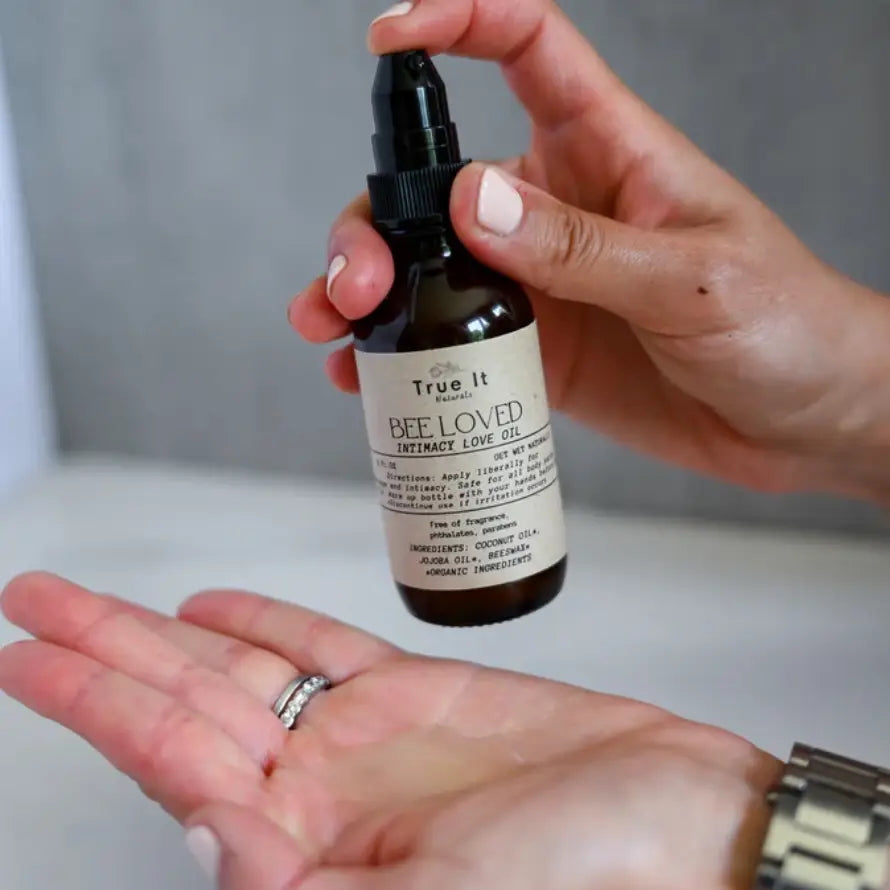 Person holding a bottle of True It Naturals Bee Loved intimacy love and massage oil with a neutral background
