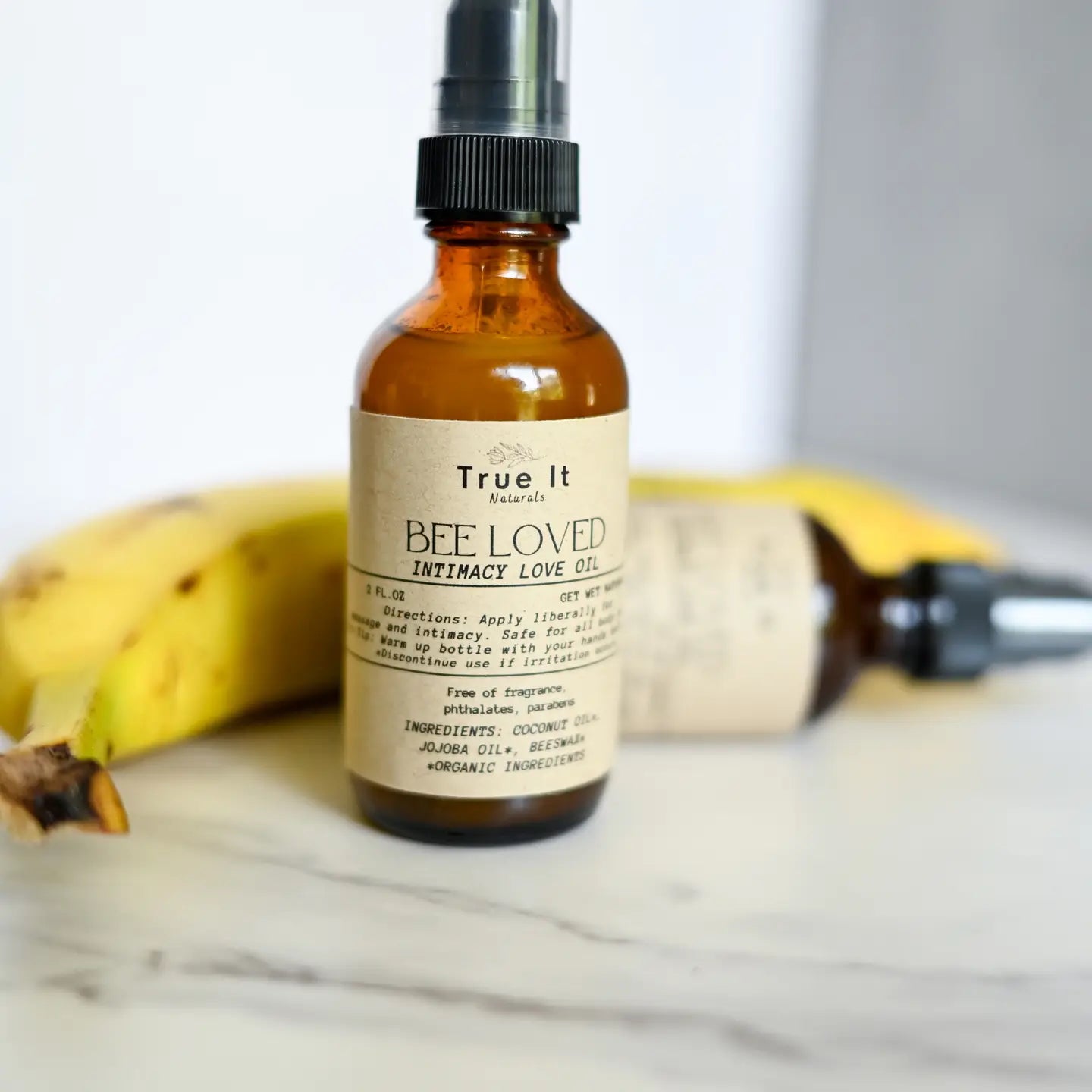 True It Naturals Bee Loved natural beeswax massage oil sitting next to a banana as a demo.