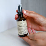 Load image into Gallery viewer, Hand holding a bottle of &#39;True It Bee Loved Intimacy Love Oil&#39; against a neutral background
