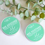 Load image into Gallery viewer, Two containers of &#39;True It&#39; Bee Soothed beeswax salve on a white background with Eucalyptus leaves.
