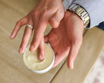 Load image into Gallery viewer, Hand applying cream from a small container on a neutral background
