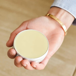 Hand holding a 2 oz beeswax salve on a beige background
