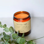 Load image into Gallery viewer, A lit True It Naturals Beeswax Candle - Vanilla Sage | 100% Beeswax, inside an amber glass jar with a wooden wick, on a light background.
