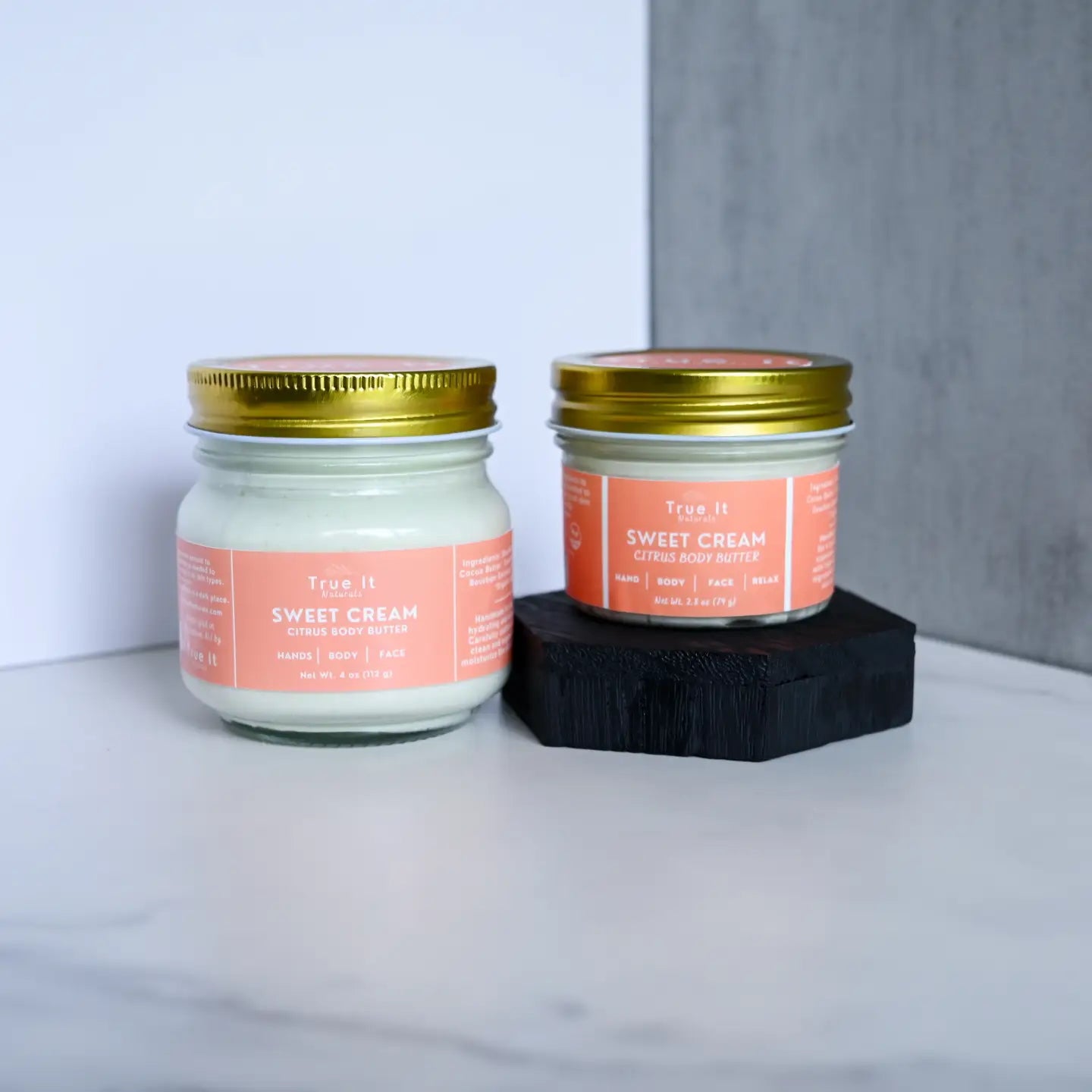 2oz small citrus cream body butter raised up next to the large 4oz citrus cream body butter
