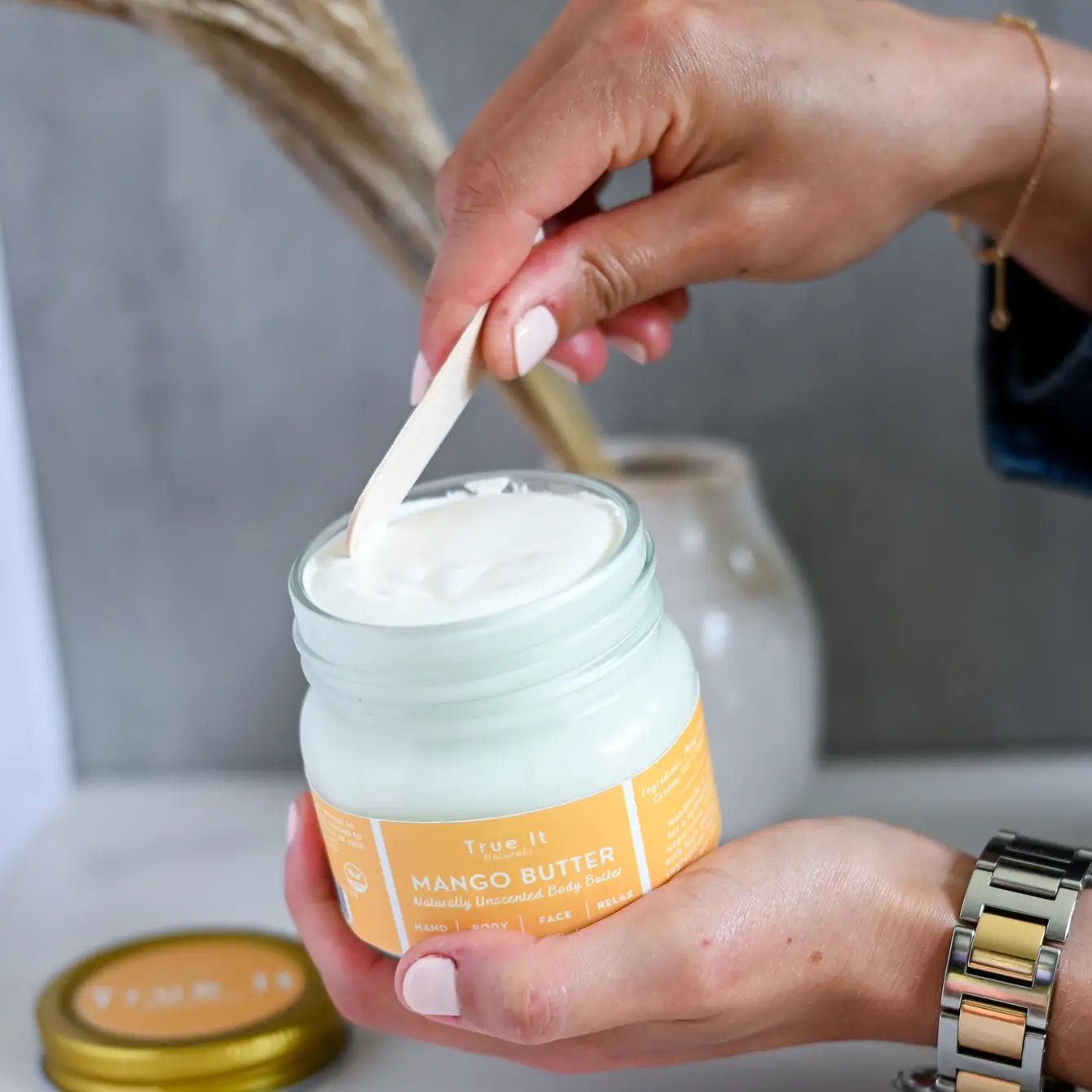 True It Naturals Mango Butter Body Butter with cap off. Scooping some of the body butter with a wooden spoon.