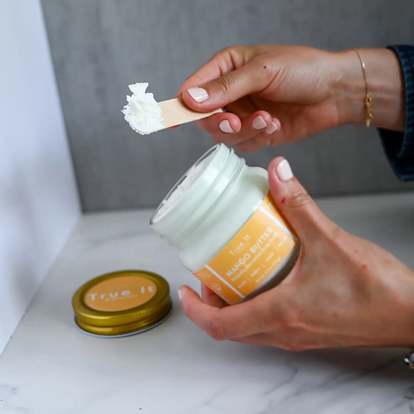 True It Naturals Mango Butter Body Butter with cap off. Scooping some of the body butter with a wooden spoon.