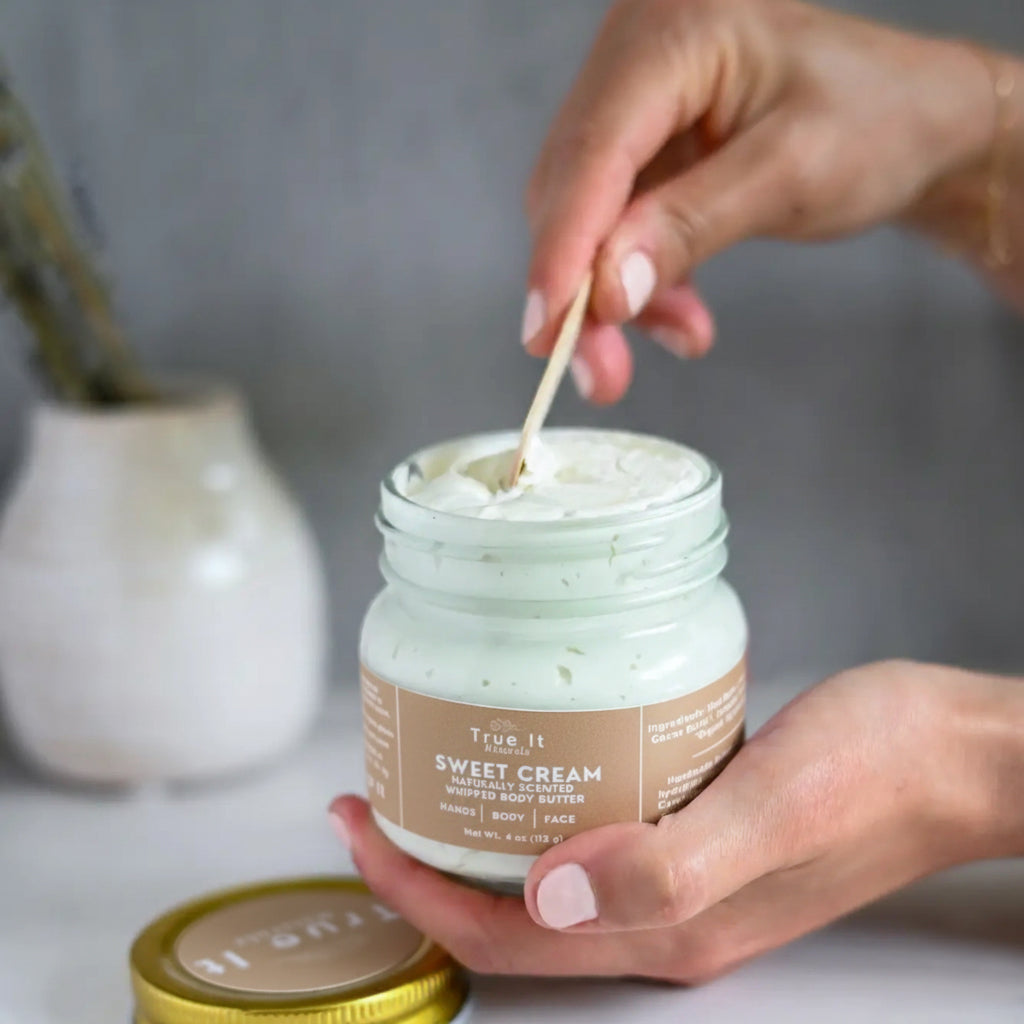 Person using a wooden spoon to scoop out cream from a jar of True It Naturals Sweet Cream whipped body butter.